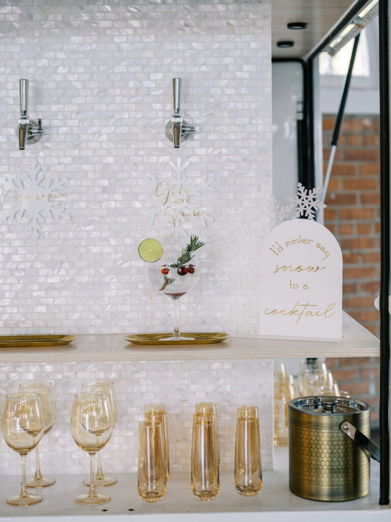 Holiday bar setup at BRICK in San Diego, California. A holiday cocktail is on display with a mint sprig and cranberry garnish, along with a sign reading I'd never say snow to a cocktail.