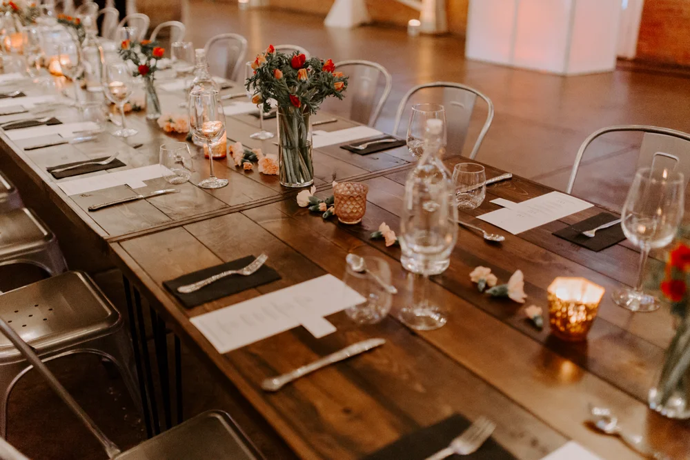 Farm tables set up family style with simple place settings and small floral arrangements for office holiday party.