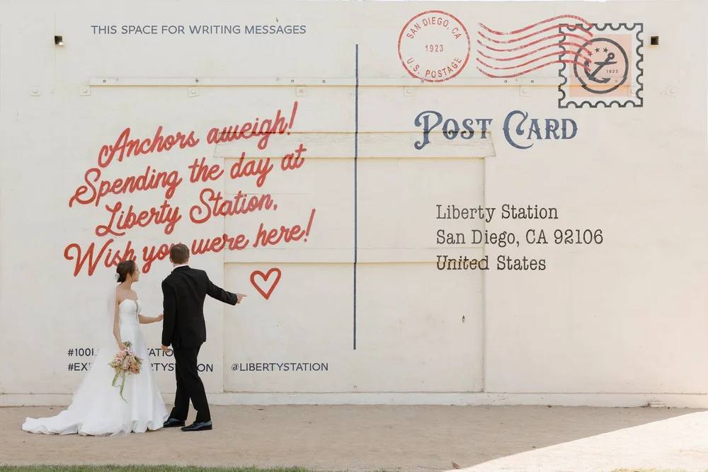 Bride and groom standing in front of a postcard mural in Liberty Station, San Diego.